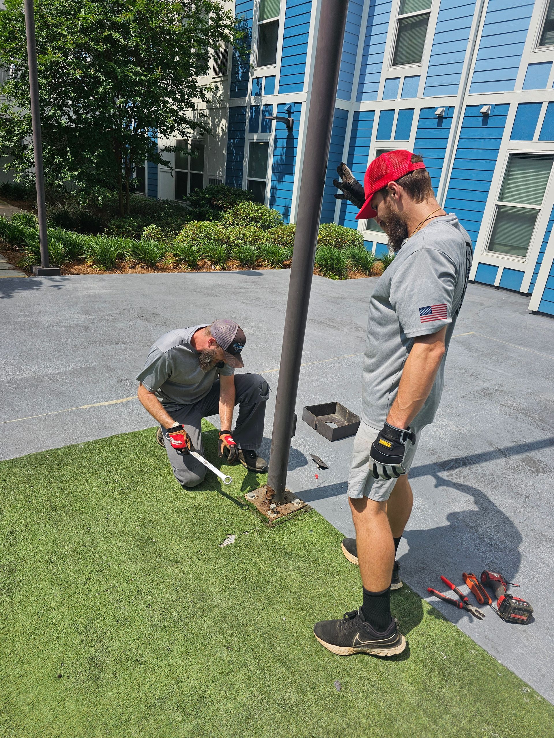 Two men are working on a pole in front of a blue building - Milton, FL - Damn Fine Jobs