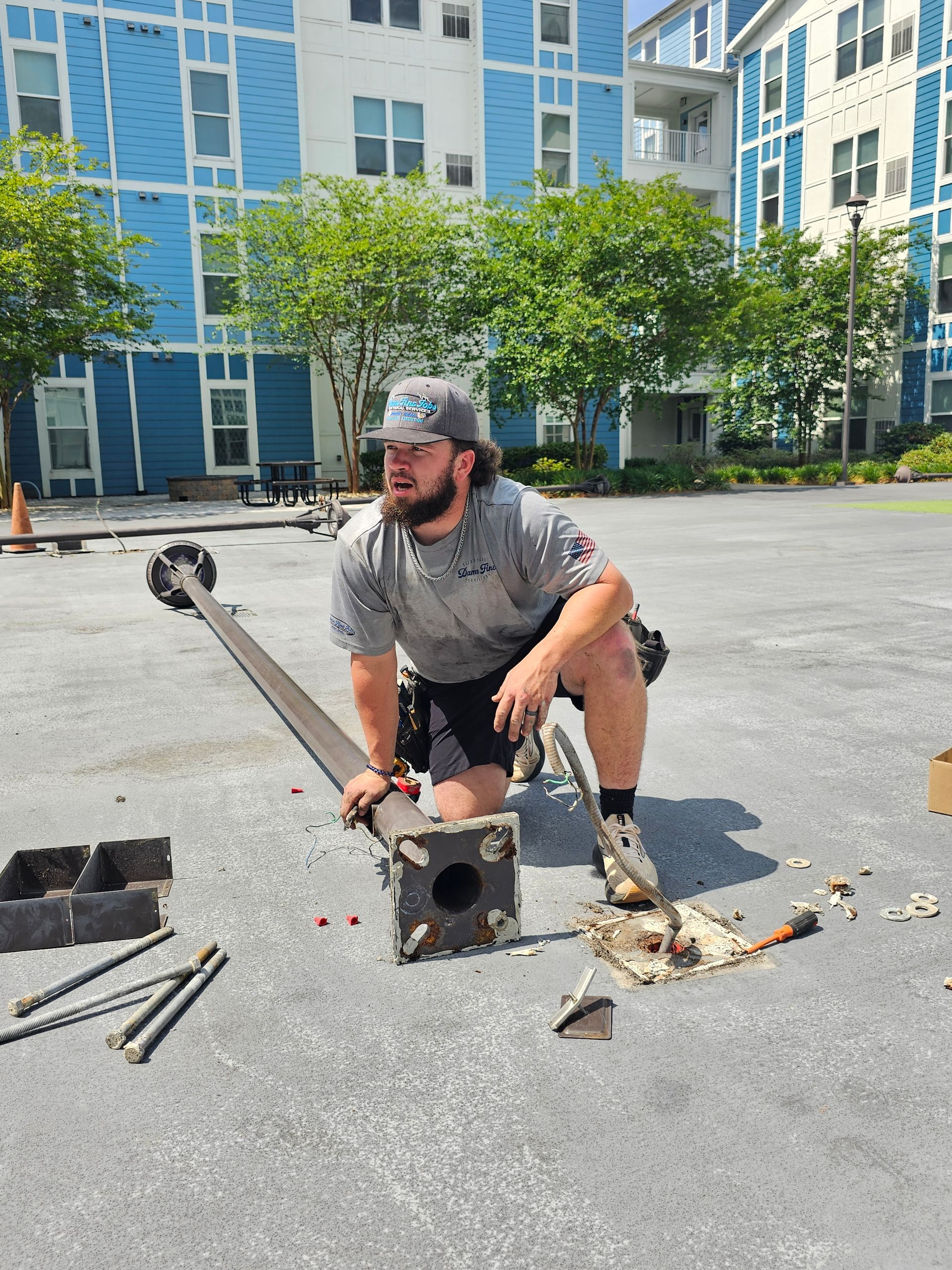 A man is kneeling down in a parking lot while working on a pole - Milton, FL - Damn Fine Jobs