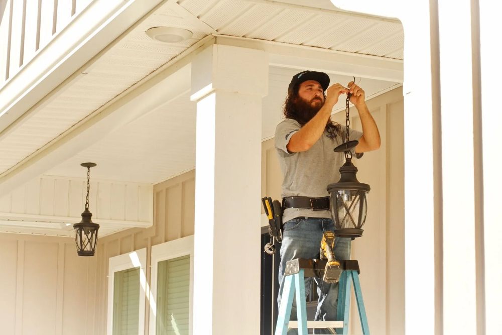 A man is standing on a ladder fixing a light on a porch - Milton, FL - Damn Fine Jobs
