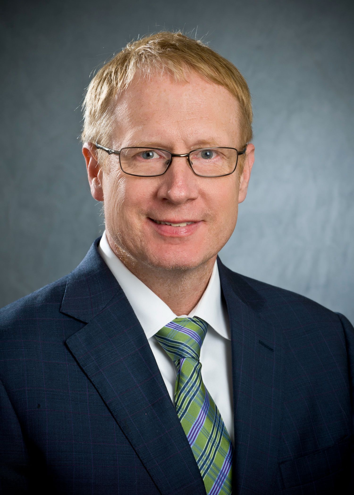 Photo of Dr. R. Michael Johnson wearing glasses, navy blue suit and a plad tie