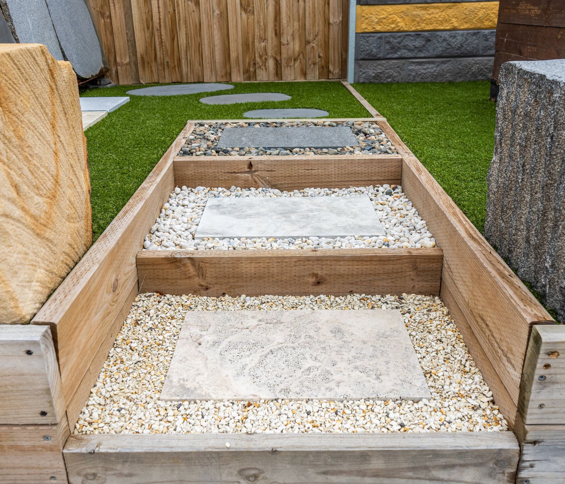 Wooden stepped garden path with gravel and square concrete pavers between stone borders