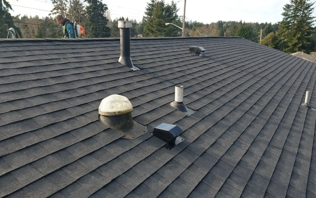 Aerial view of newly installed gray asphalt shingle roof with vent pipes and chimney caps