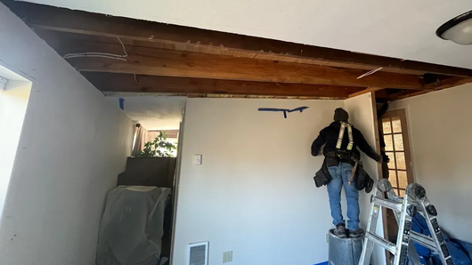 Contractor on ladder working on wood beam ceiling during interior remodel