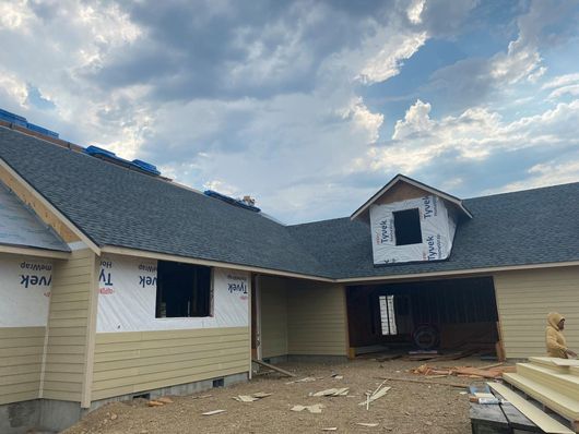 Front view of new home construction with installed shingle roof and siding in progress