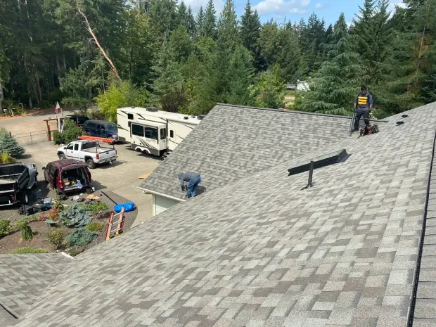 Aerial view of completed shingle roof installation with roofer working near RV and driveway