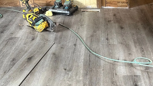 Wood-look laminate flooring installation with tools and materials on subfloor