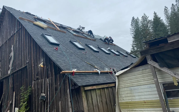 Roofing crew actively tearing off and replacing barn roof shingles with skylights exposed during installation
