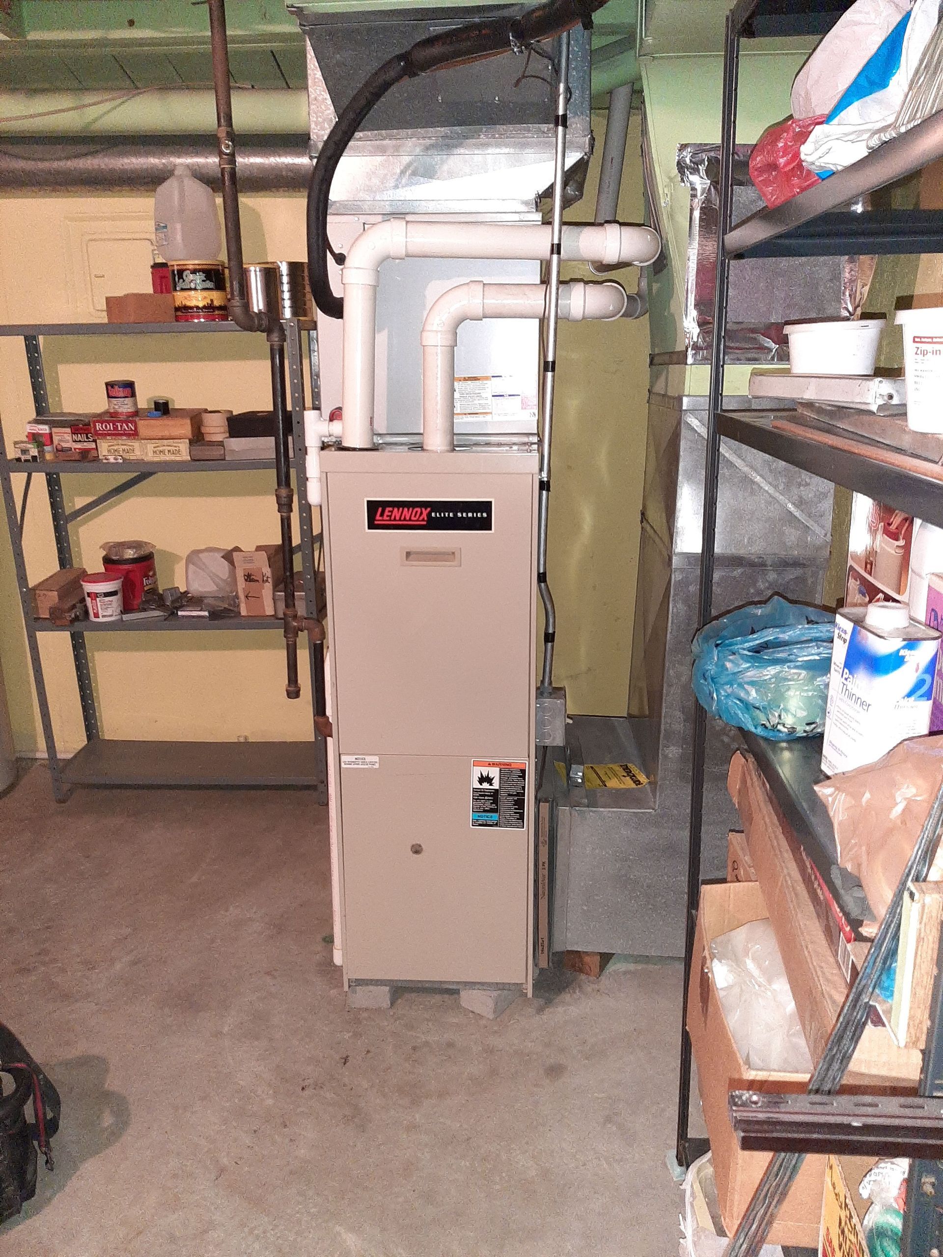 Furnace in a basement surrounded by shelves with items.