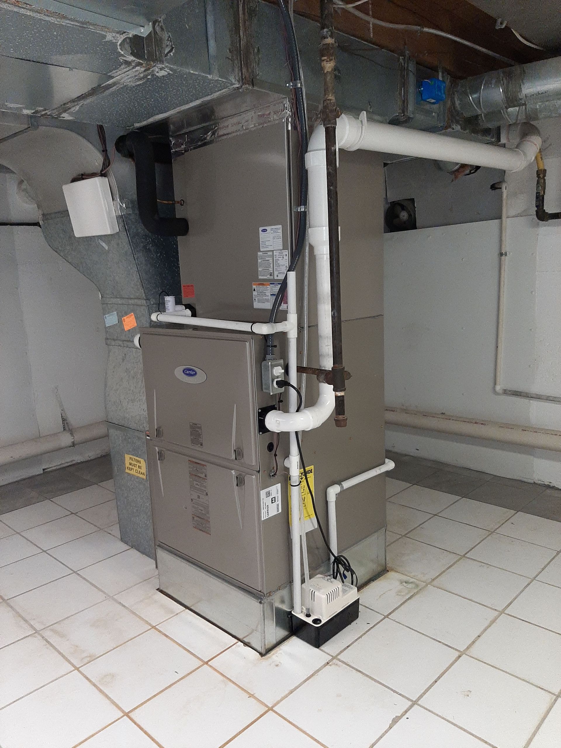 A central heating and air conditioning unit installed in a basement, with associated ductwork and pipes.