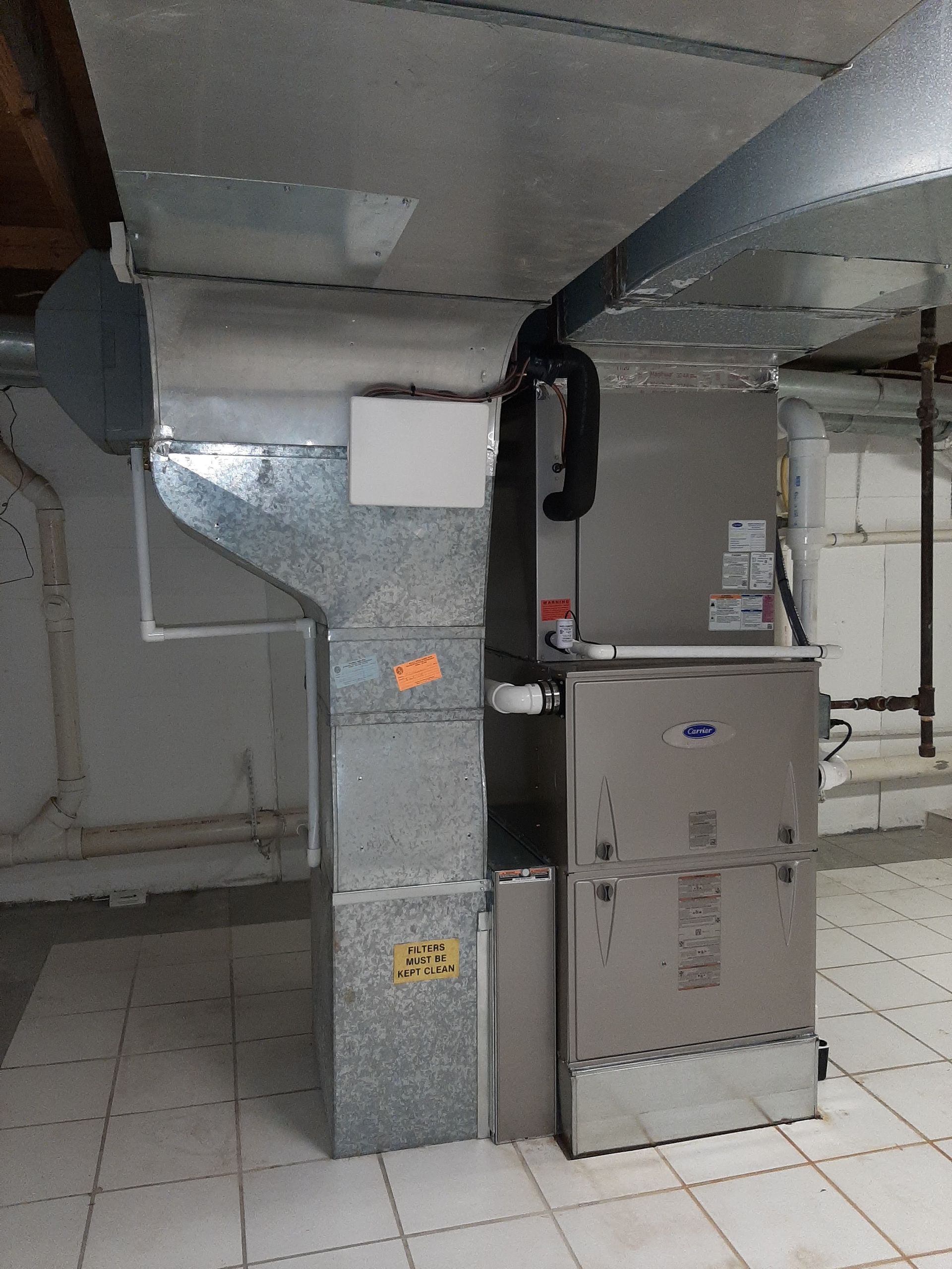 Furnace and ductwork in a basement. Silver metal unit with attached vents.