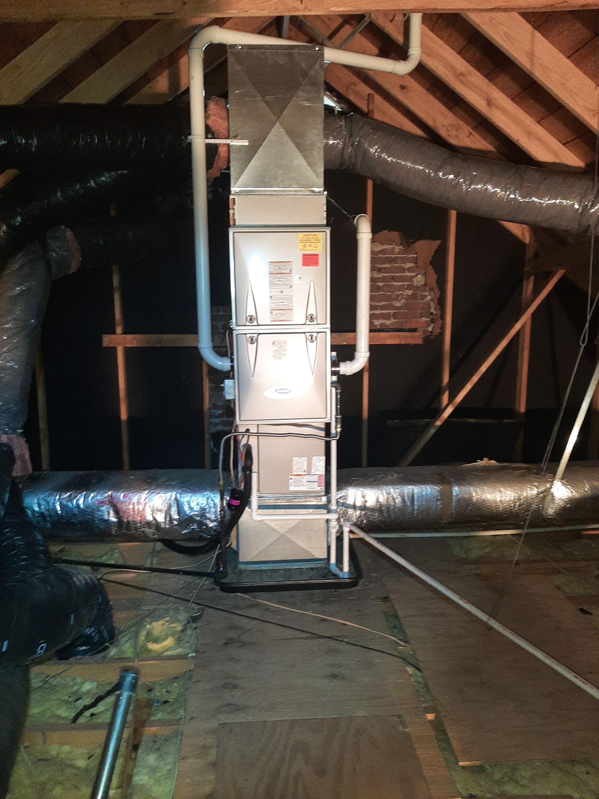 HVAC unit in an attic with insulated ductwork and wooden beams.