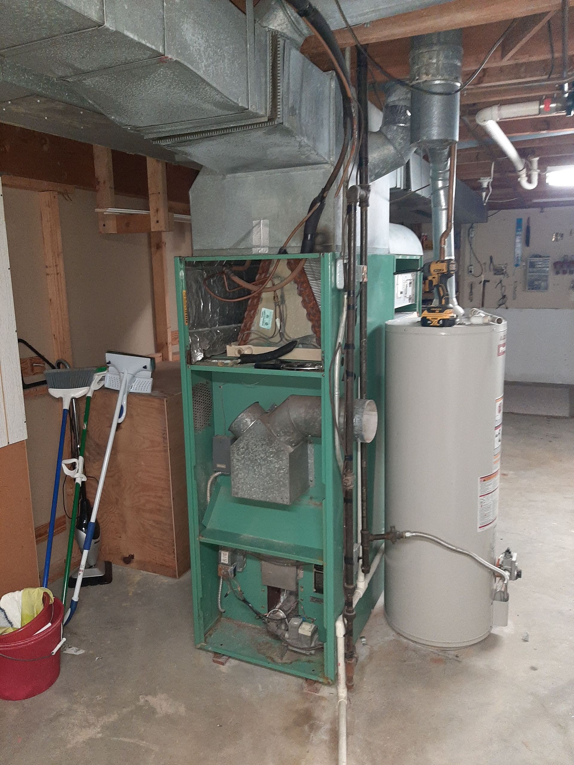 Green furnace and water heater in a basement. Ductwork and pipes are visible.