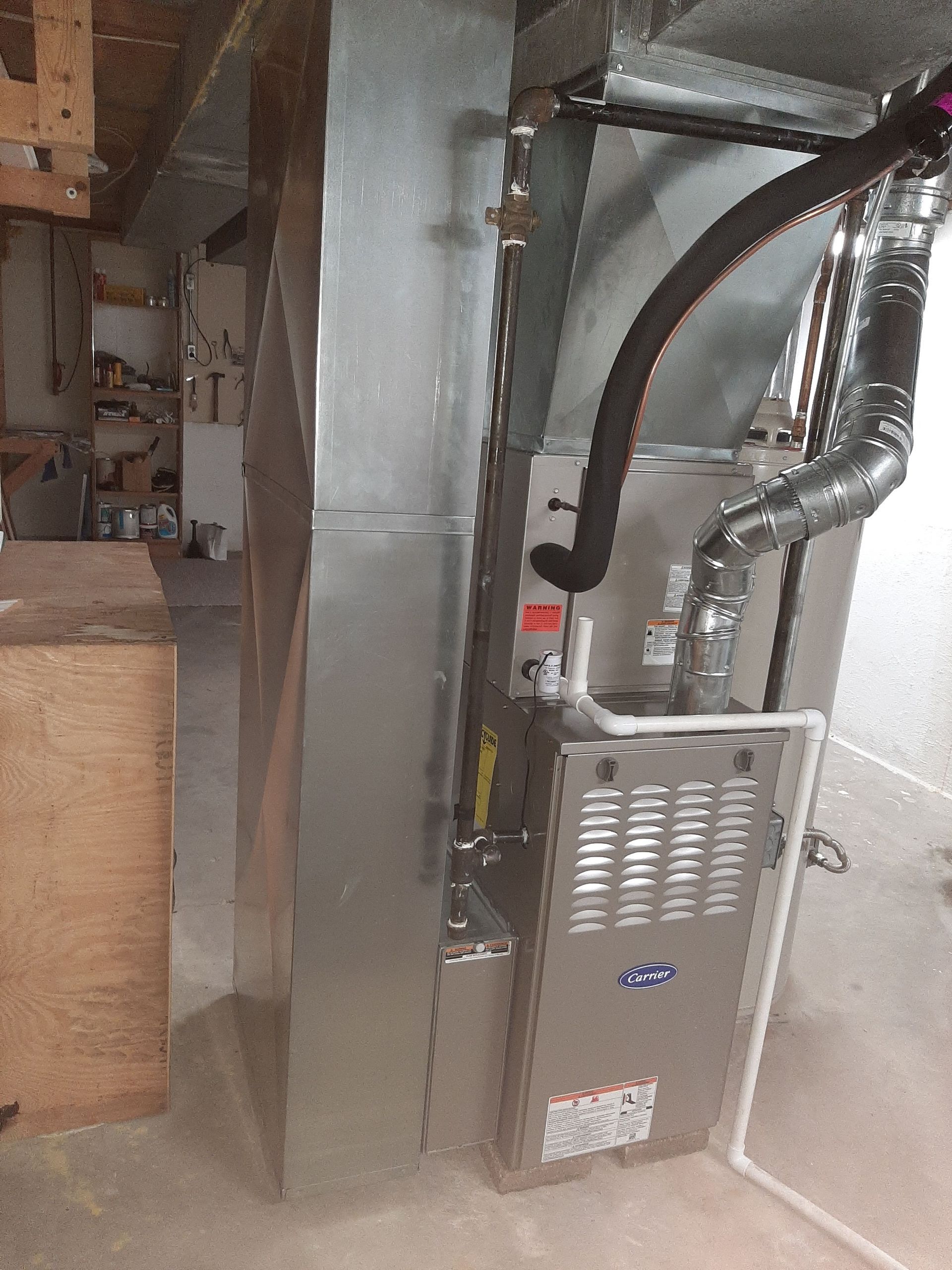Silver furnace and ductwork in a room with a concrete floor and a wooden cabinet.