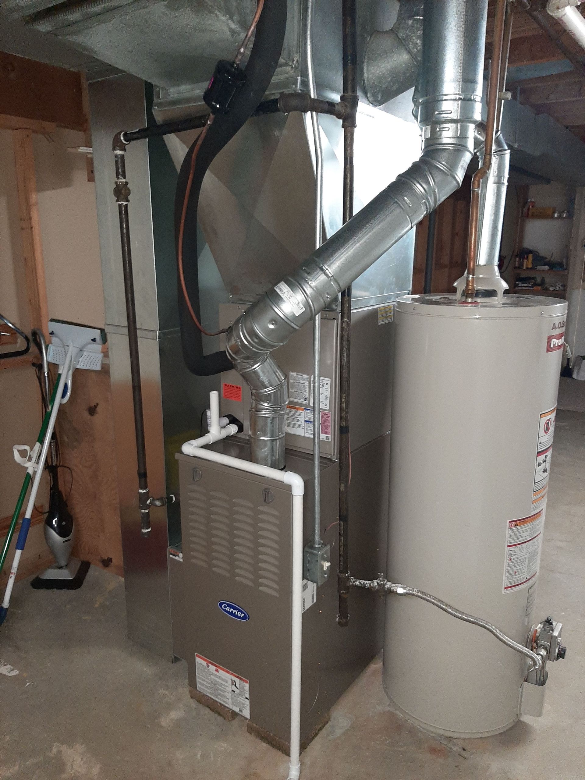 Furnace and water heater in a basement. Silver metal appliances with pipes and vents.