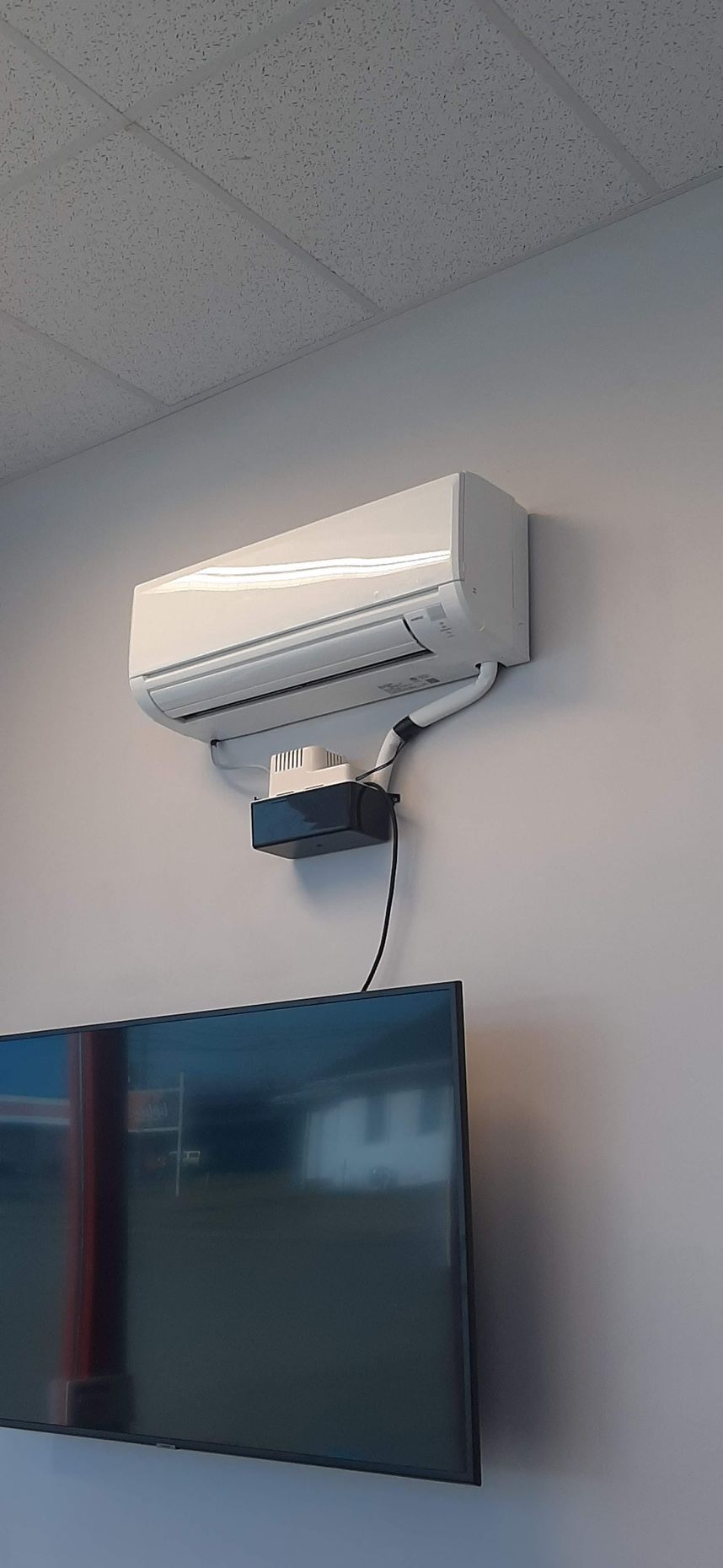White air conditioning unit mounted on a wall above a television.