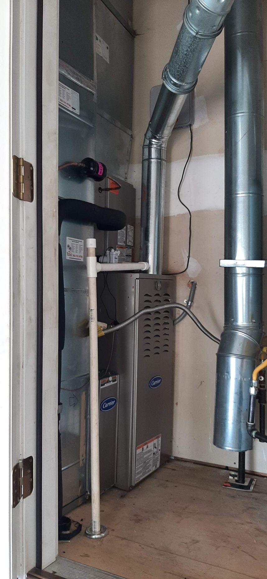 A gas furnace installed in a utility closet with vent pipes and a condensate drain.