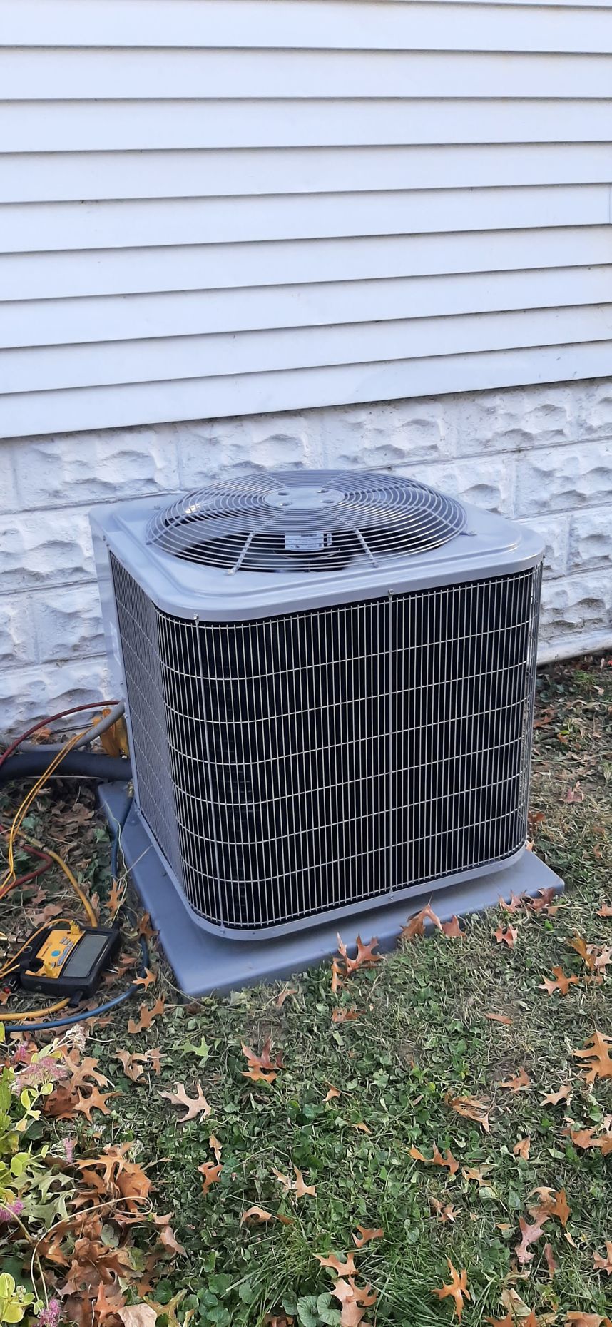 Air conditioning unit outdoors, next to a house with white siding and a brown lawn.