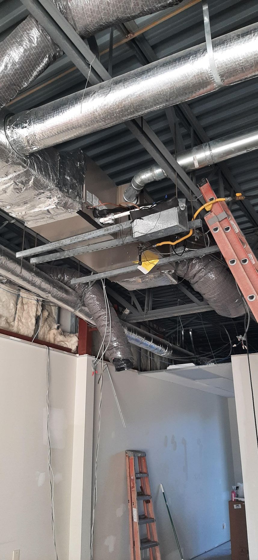 Interior view of a construction site ceiling. Ductwork, exposed beams, and a ladder are visible.