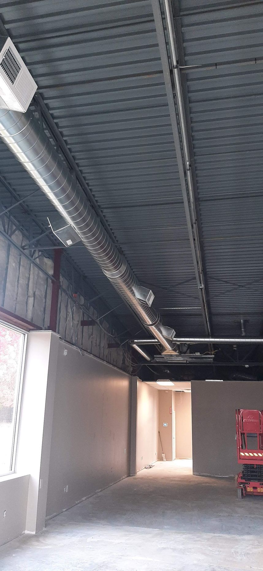 Interior of a building under construction, showing metal ceiling, ductwork, and unfinished walls.