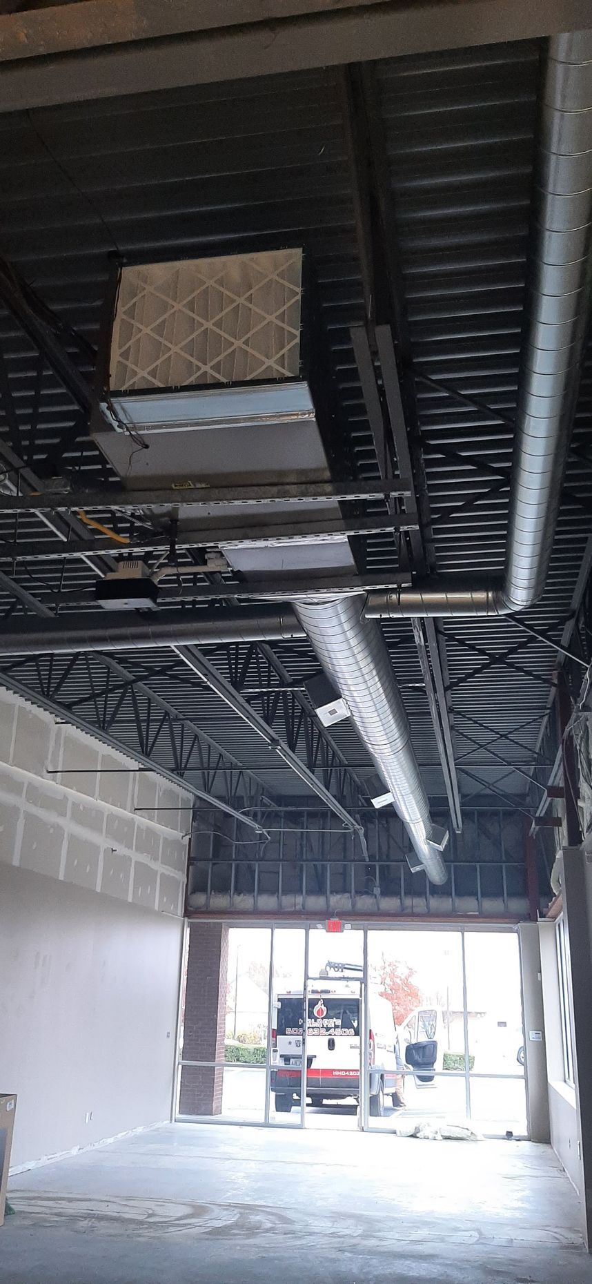 Interior view of a building under construction. Ceiling beams, ductwork, and open doorway.