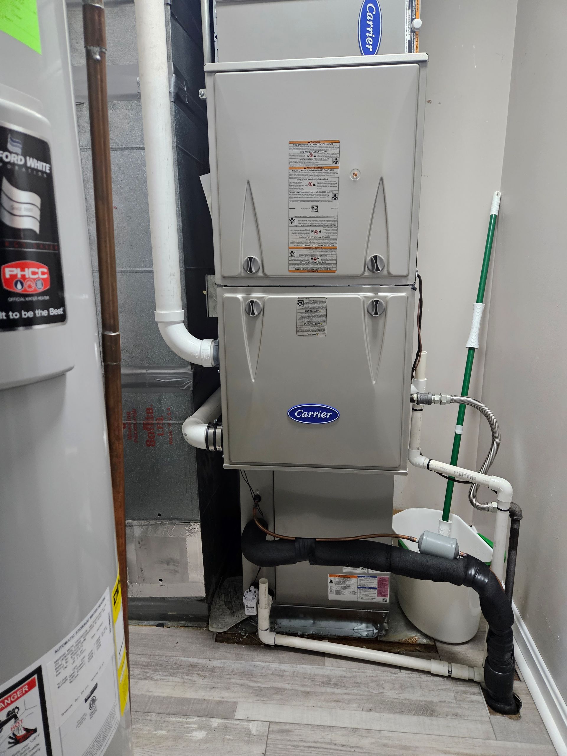 A Carrier HVAC system and water heater in a utility room. White pipes and a black drain line visible.