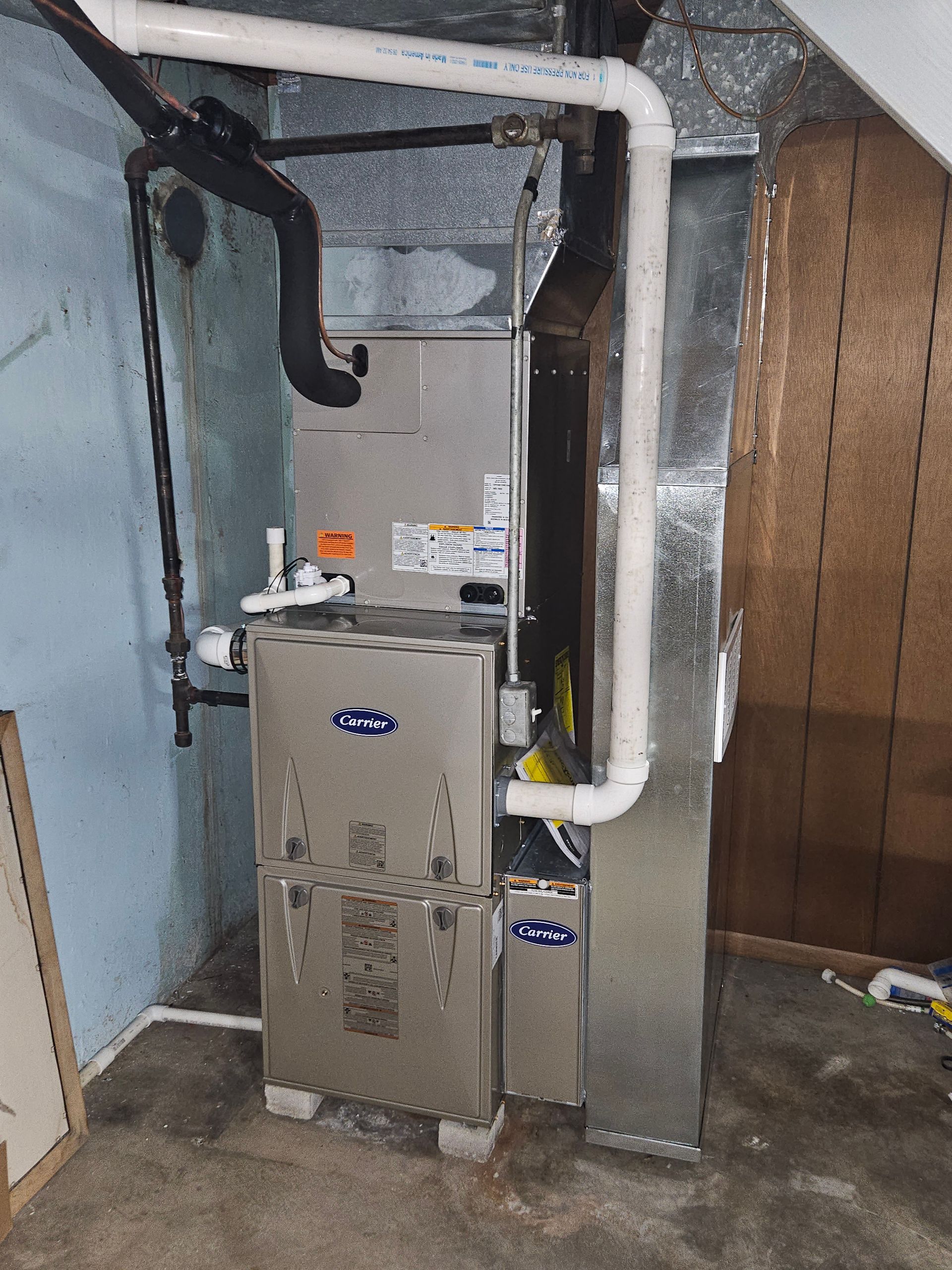 Furnace in a basement, silver metal, with white pipes and ductwork.