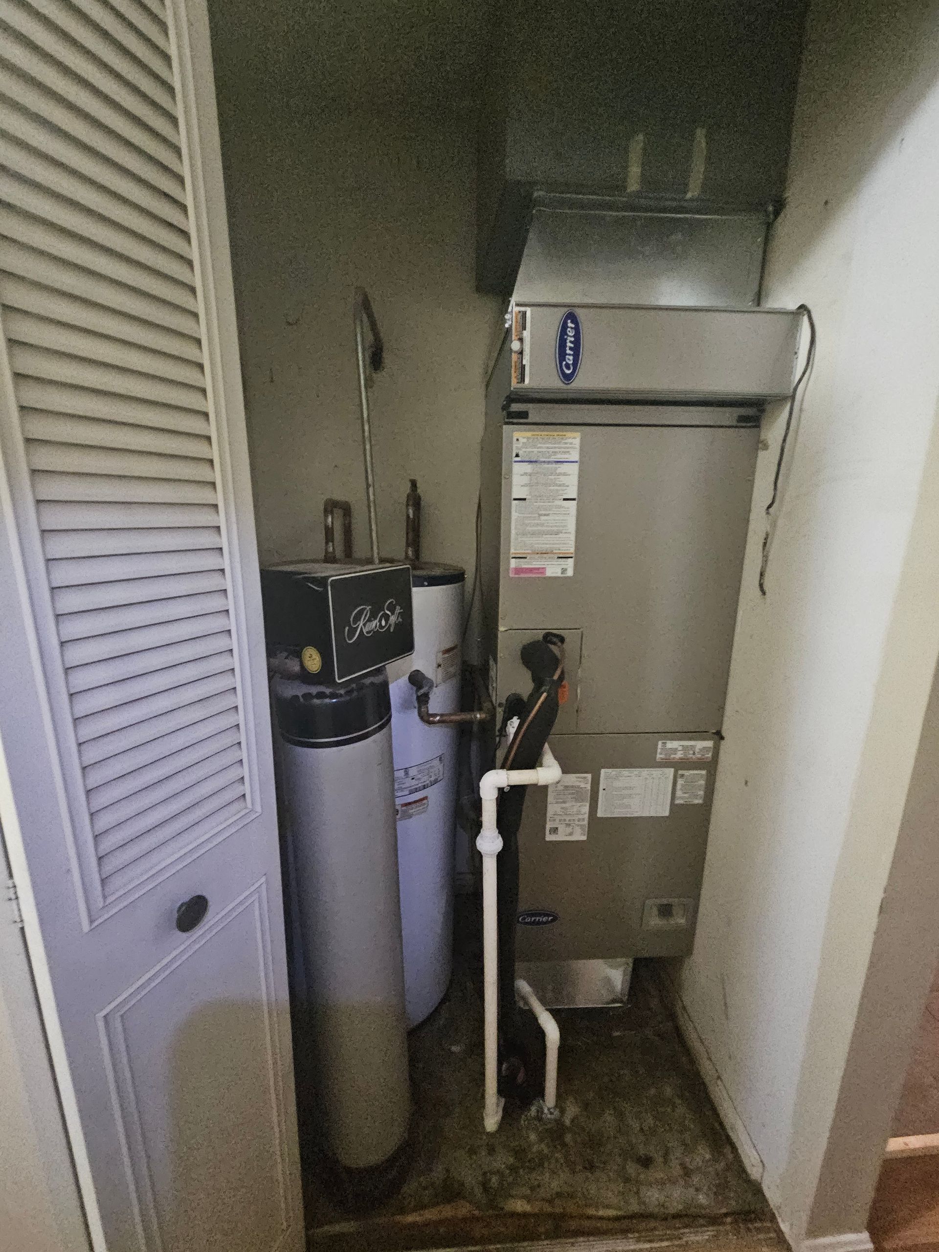 A utility closet with a water heater, furnace, and a tall, white water tank.