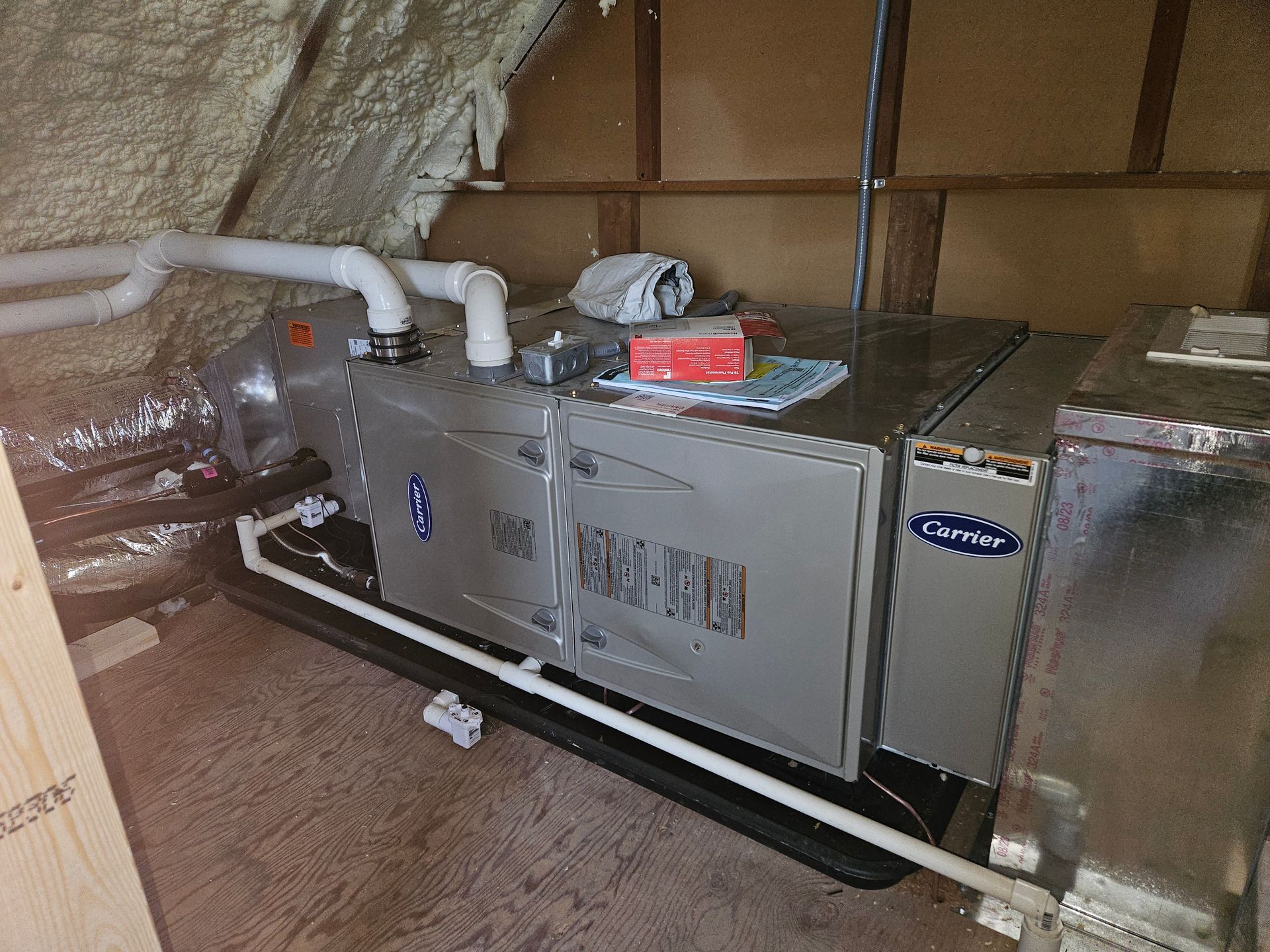 HVAC unit in an attic with white pipes and ductwork, on a black base.