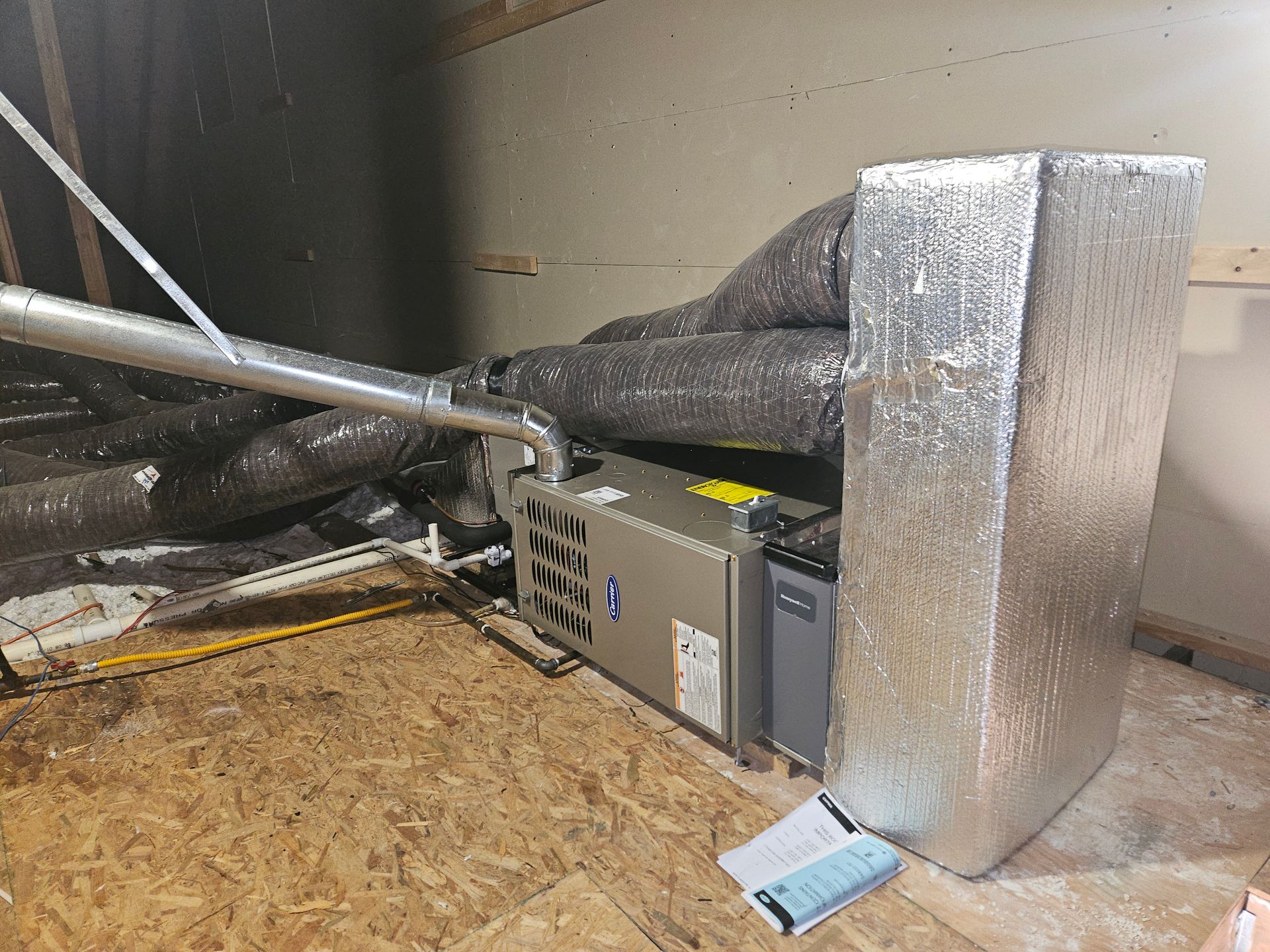 Furnace in an attic with insulated ductwork and a rectangular metal enclosure.