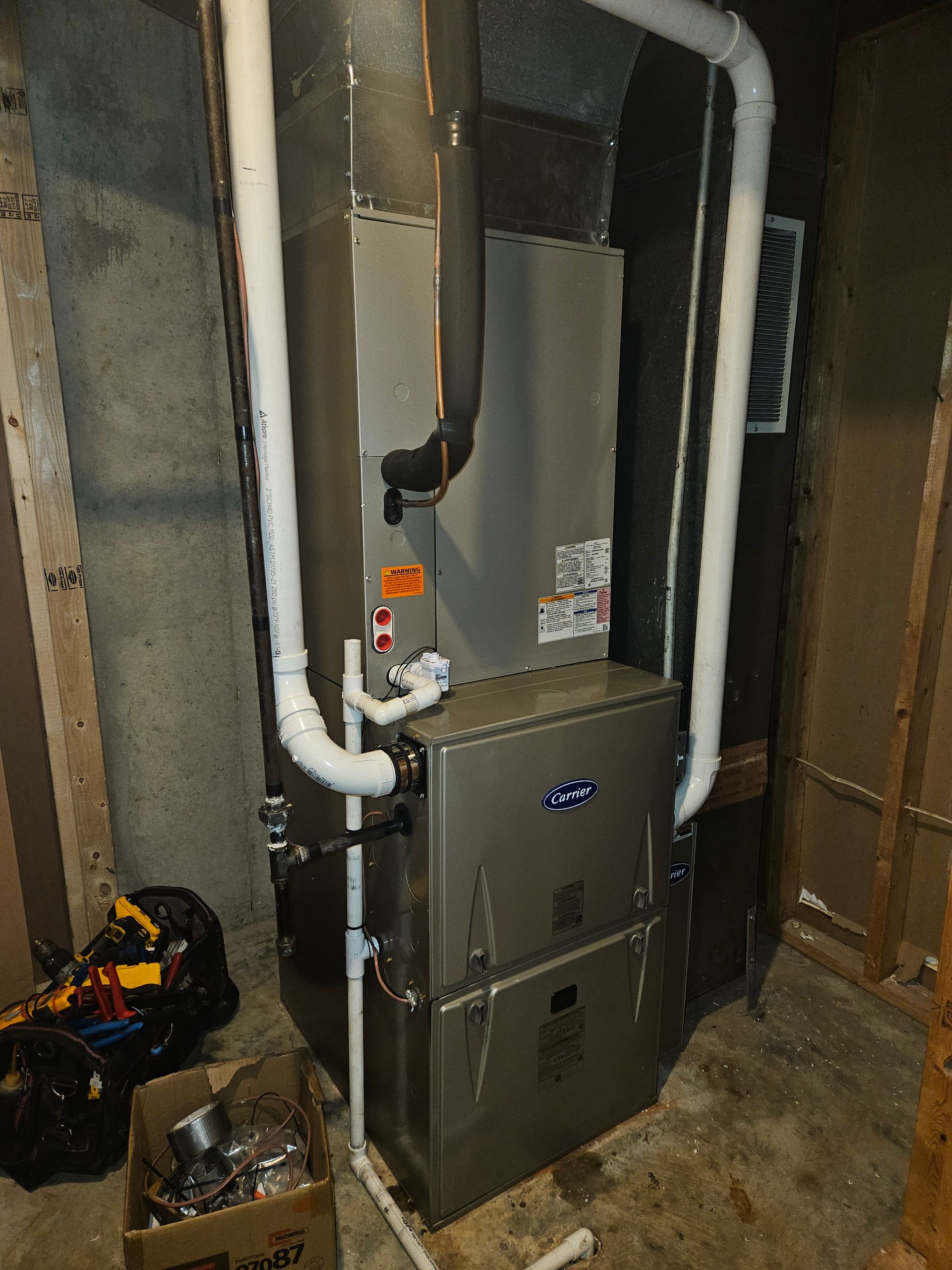 Furnace in a basement. Ductwork, pipes, and some tools are visible.
