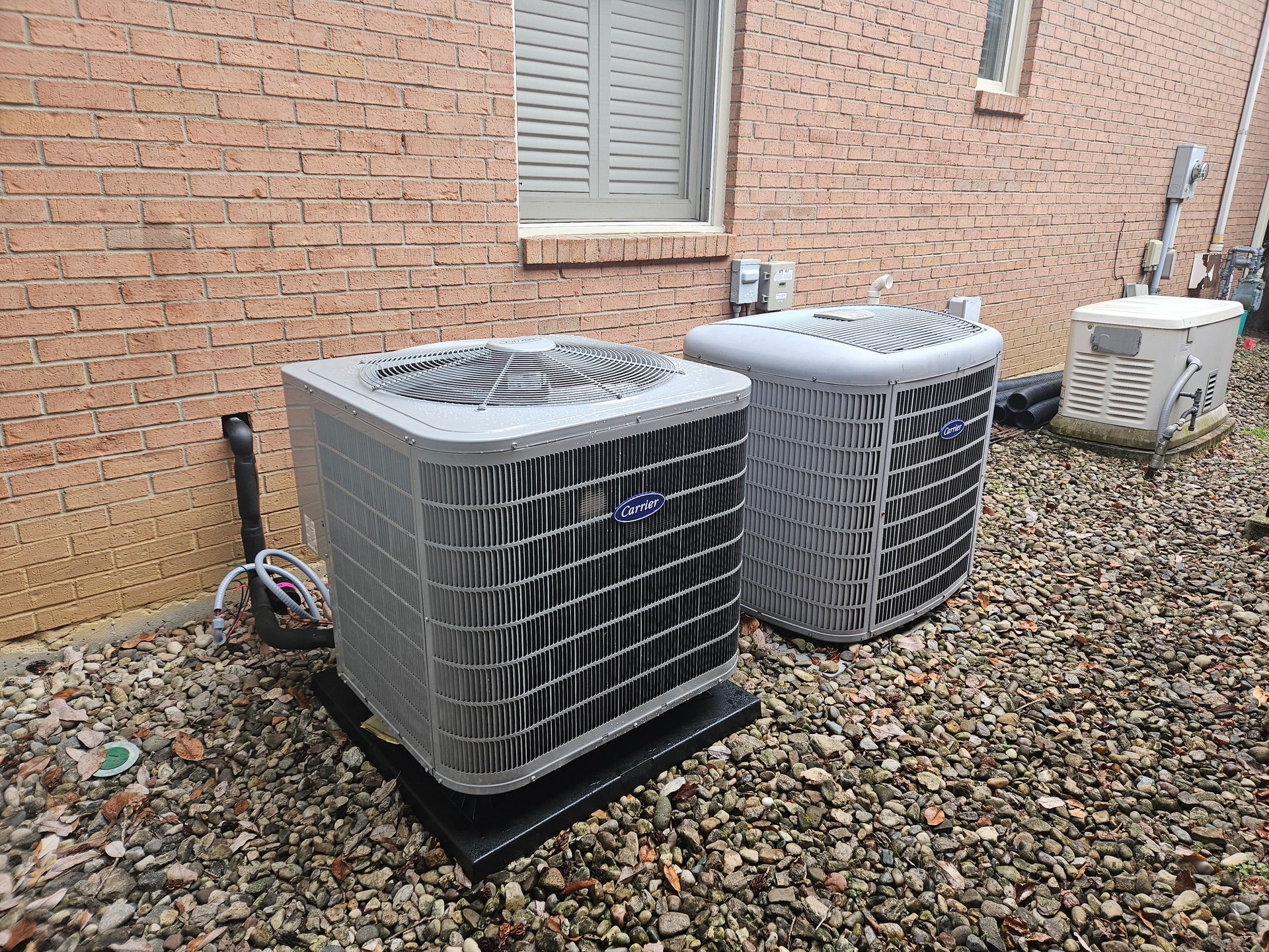 Two central air conditioning units outside a brick building on gravel.