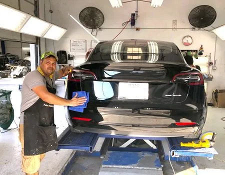 Mechanic polishing the rear of a black SUV in an auto repair shop
