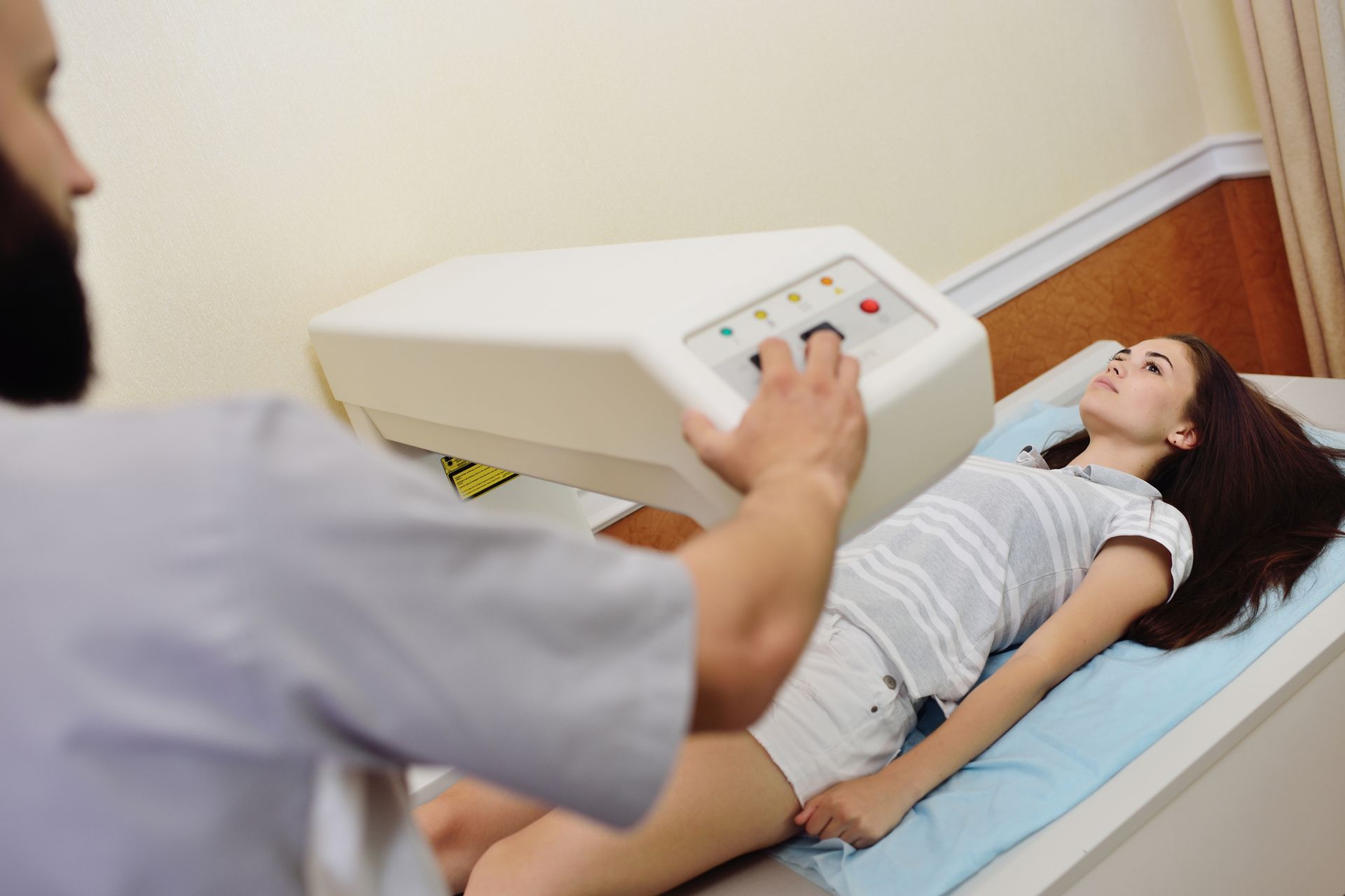 A woman is laying on a bed getting an x-ray from a doctor.