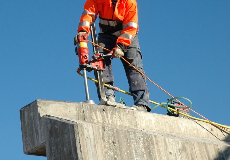 A man in an orange jacket is using a machine to cut concrete