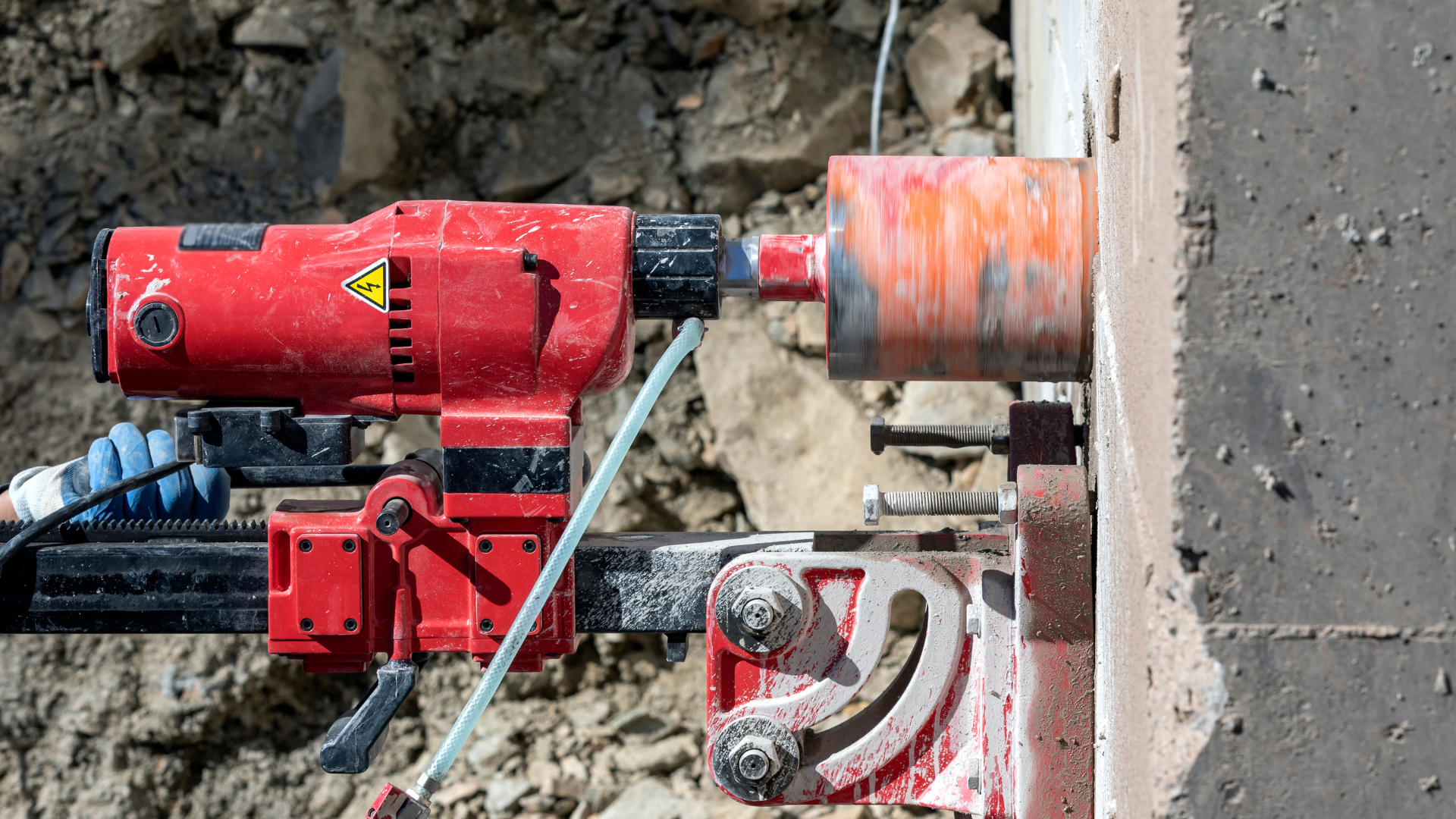 A red drill is cutting a hole in a concrete wall.