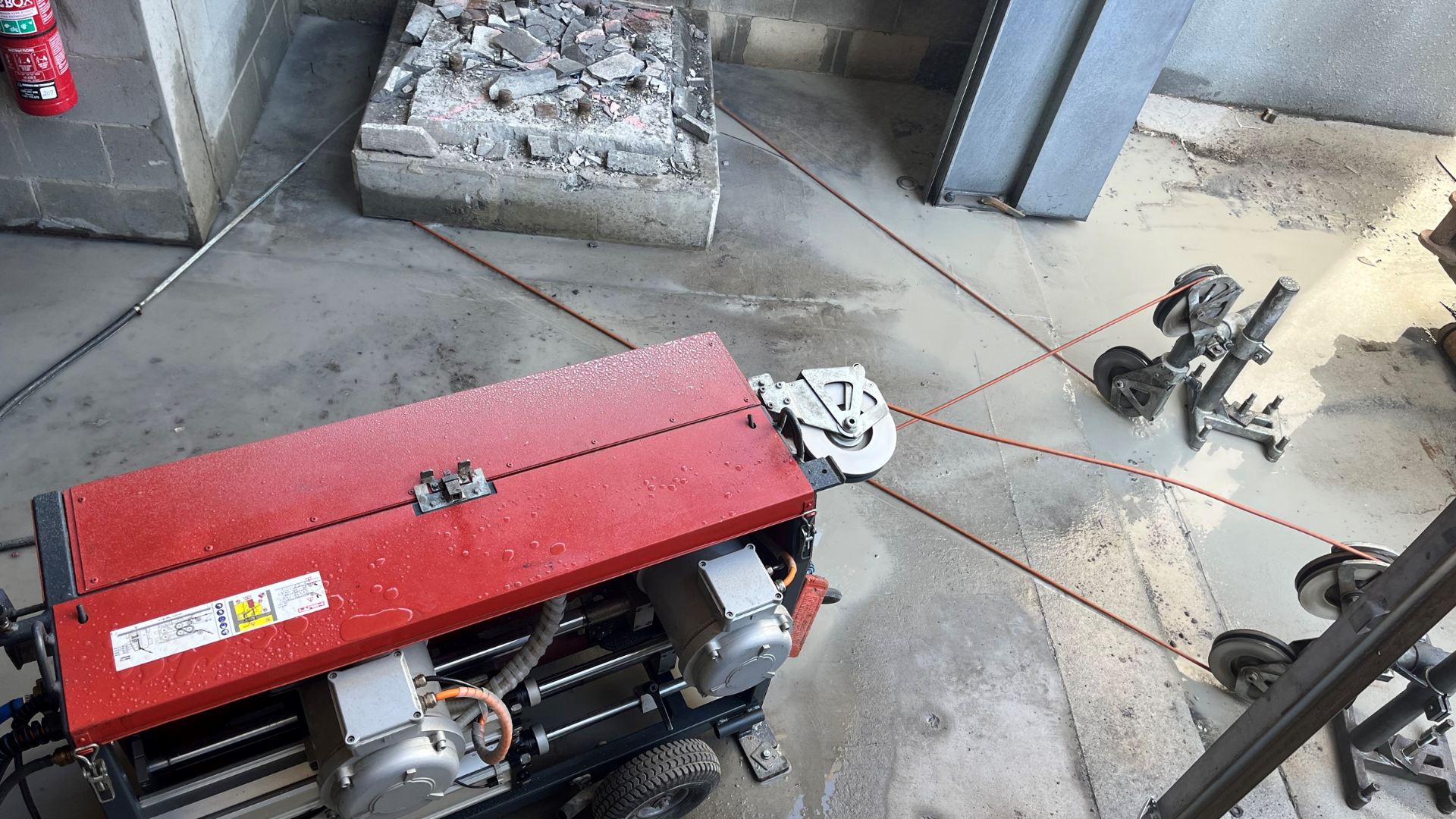 A red machine is sitting on the floor next to a fire extinguisher.