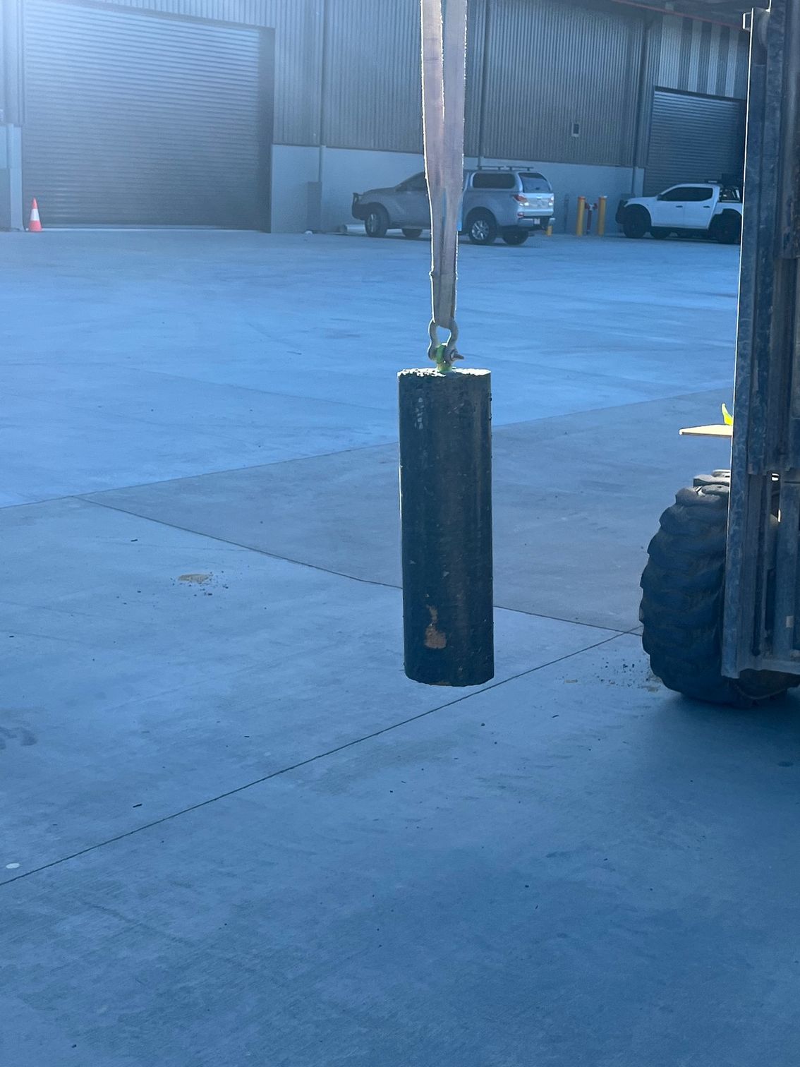 A forklift is parked in a parking lot with a large black object hanging from it.
