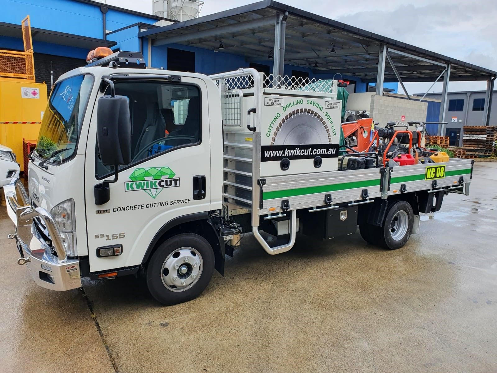 A white truck with a green logo on the side is parked in front of a building.