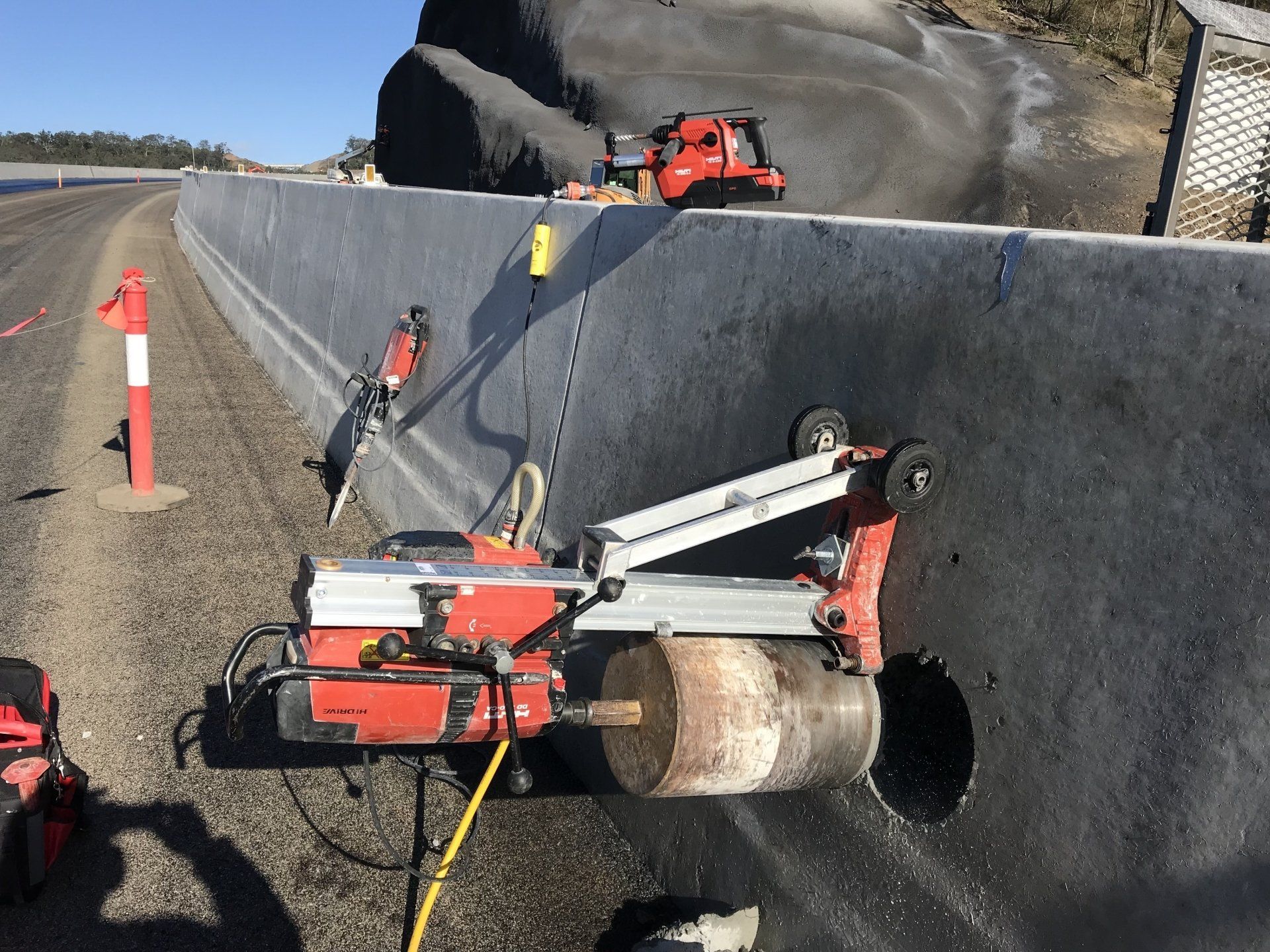 A machine is cutting a hole in a wall on the side of a road.