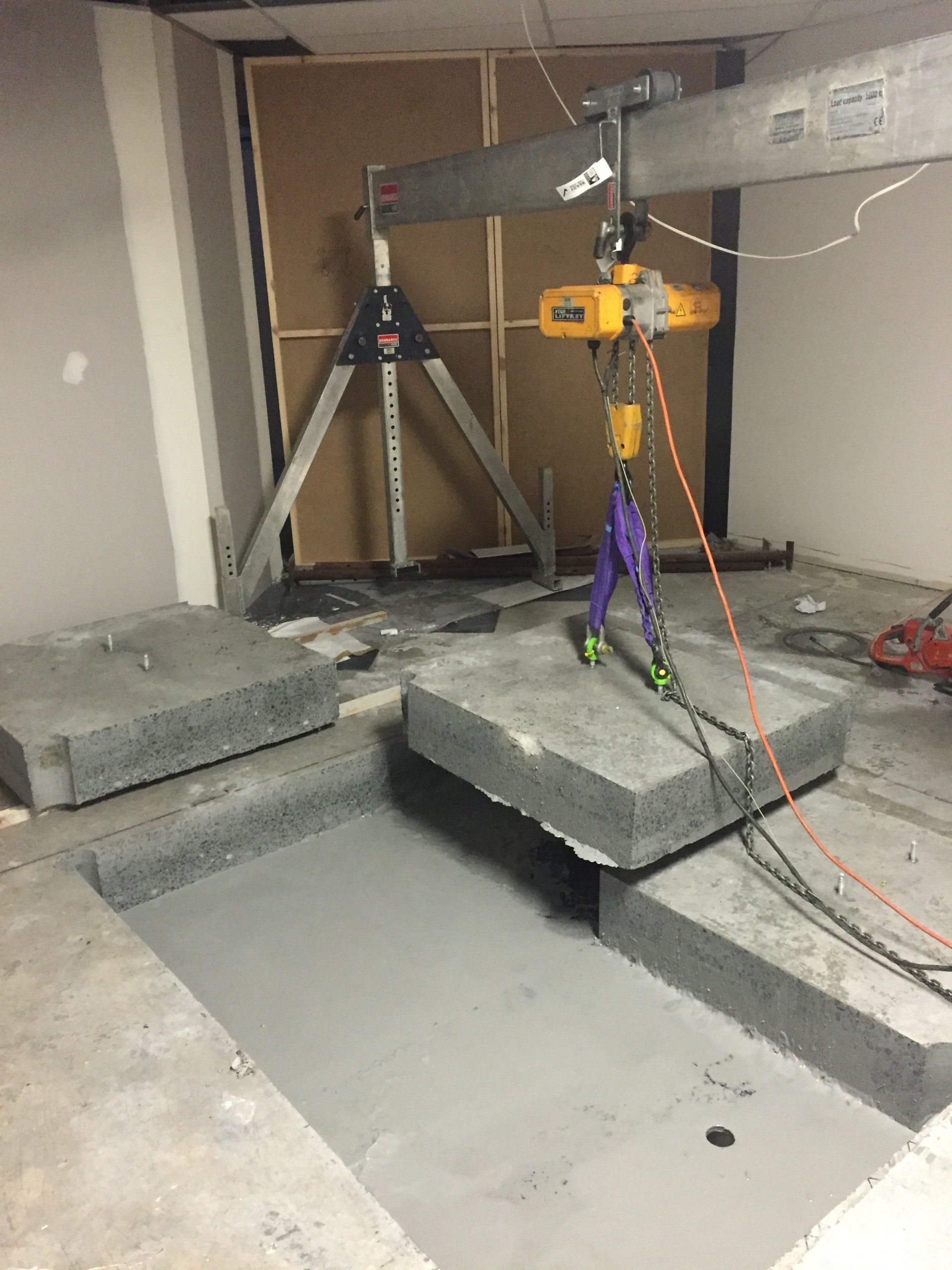 A concrete slab is being lifted by a crane in a room.