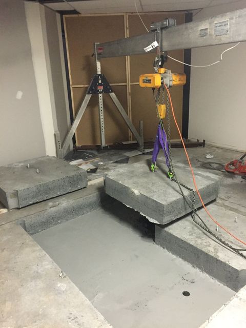 A concrete slab is being lifted by a crane in a room.