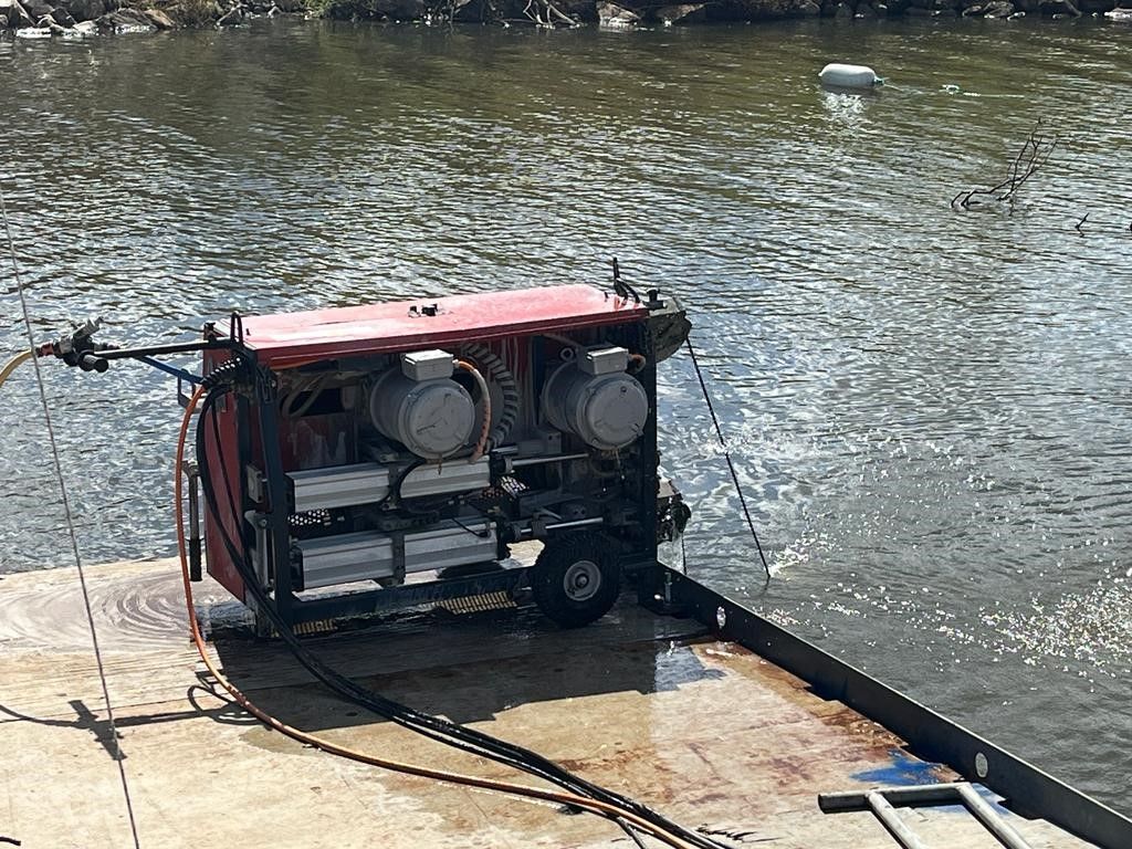A red generator is sitting on a dock next to a body of water.