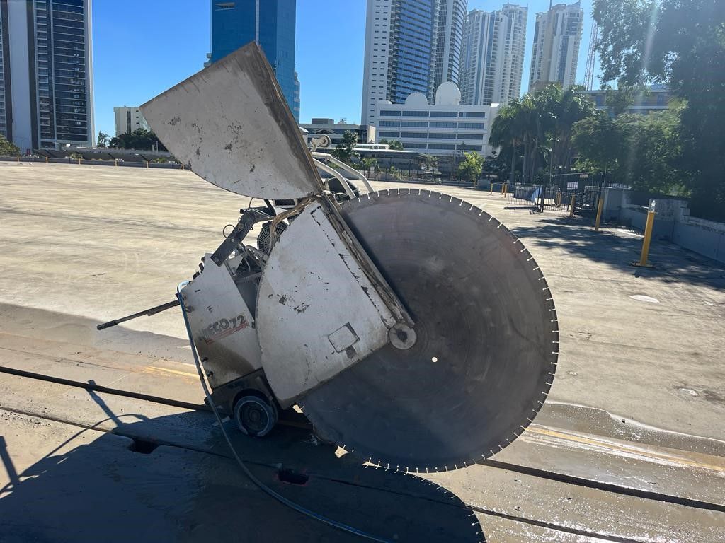 A large circular saw is cutting concrete on a city street.