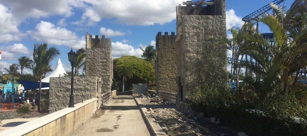 A stone wall with a castle in the background and palm trees in the foreground.