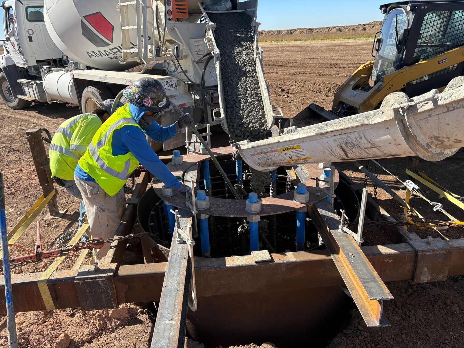 Workers pouring concrete from a truck into a steel-framed structure at a construction site.