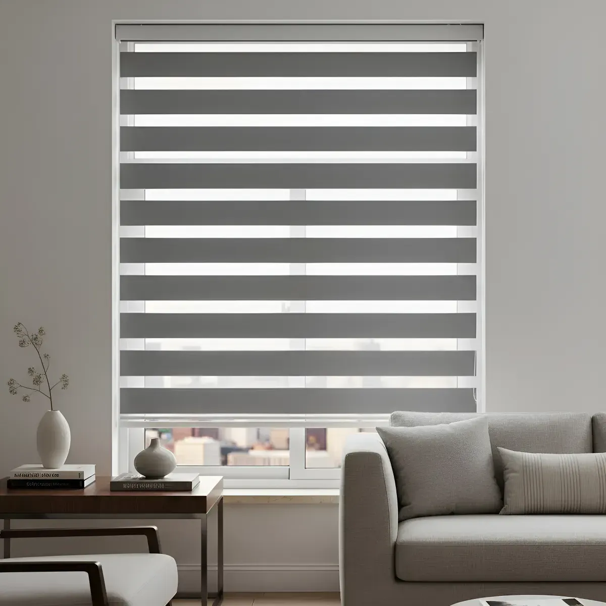 Persianas enrollables de cebra grises y blancas en una ventana de una sala de estar, con un sofá gris y una mesa auxiliar.