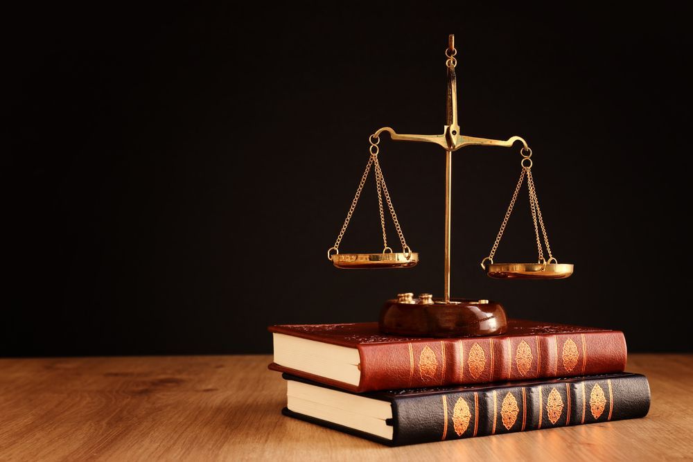 A golden scale of justice sits atop two law books on a wooden surface, against a black background.