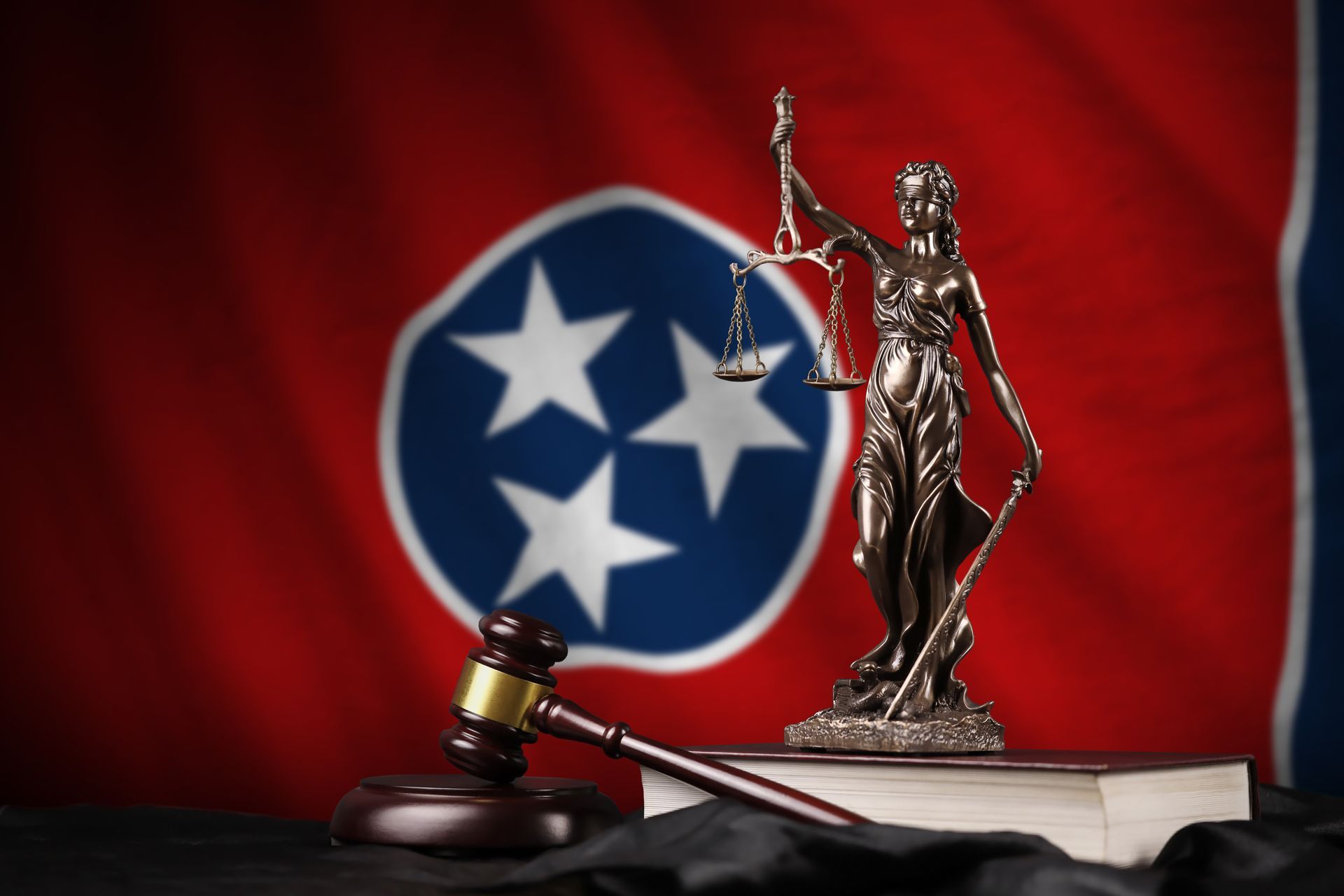 A statue of Lady Justice holding scales and a gavel resting in front of the Tennessee flag.