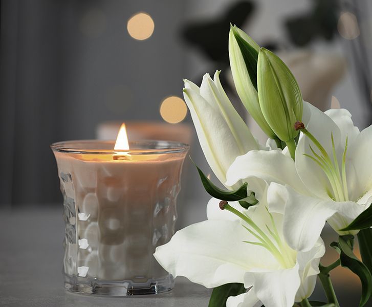 A candle is lit next to a white flower on a table.