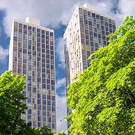 Two tall buildings are surrounded by trees on a sunny day.